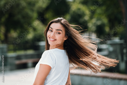 Cuadro en lienzo Smiling young woman with flowing brown hair outdoors, turning for a candid portr