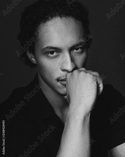 Closeup portrait of a handsome afro american young man,  touches his face with his hands, looking at camera. Black and white image.