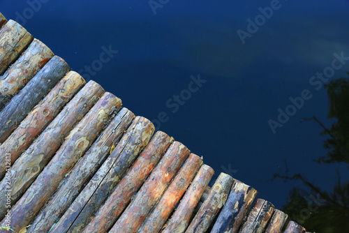 Rustic wooden logs forming a pathway over dark blue water surface