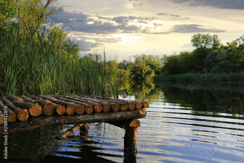Rustic wooden pier on a tranquil river at sunset with lush green reeds