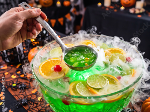 Hand holding ladle with spooky green Halloween party punch and dry ice smoke over a glass bowl