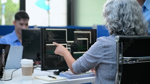 Senior Asian female software engineer coding on a desktop computer while a team member manages project tasks on an agile scrum board