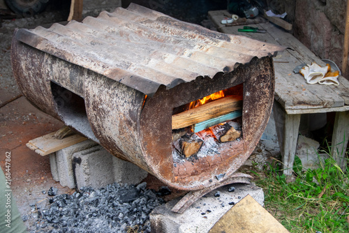 Traditional bread baking inside a rustic wood-fired barrel oven next to burning logs and hot embers. Authentic outdoor baking process in a rural village setting.