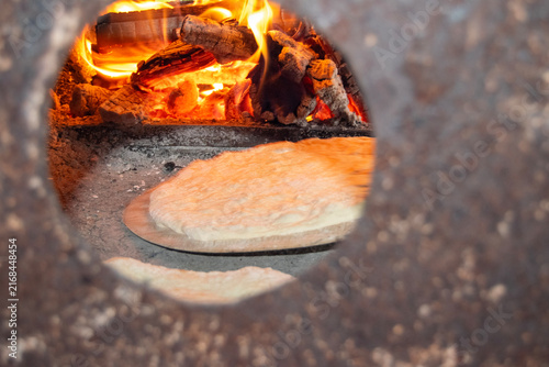 Traditional bread baking inside a rustic wood-fired barrel oven next to burning logs and hot embers. Authentic outdoor baking process in a rural village setting.