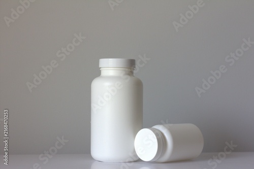 Large blank white plastic medicine bottle standing on a clean white background with a matching smaller bottle lying beside it
