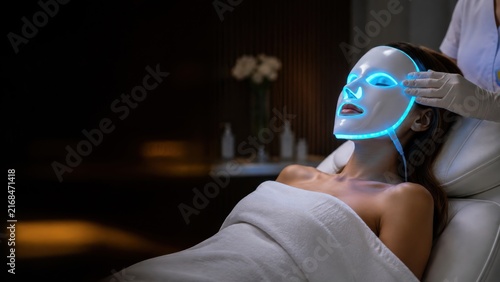 Relaxed woman undergoing futuristic LED light therapy facial treatment in spa environment