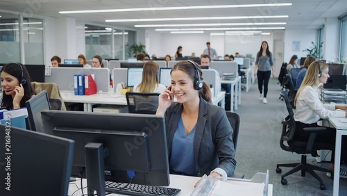 Professional women working in busy modern office environment with computer workstations and headsets
