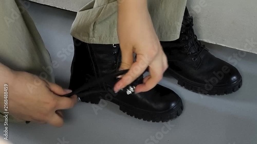 Woman attaching anti-slip ice grips to black boots before leaving home, winter safety, walking on icy roads and preventing slips.