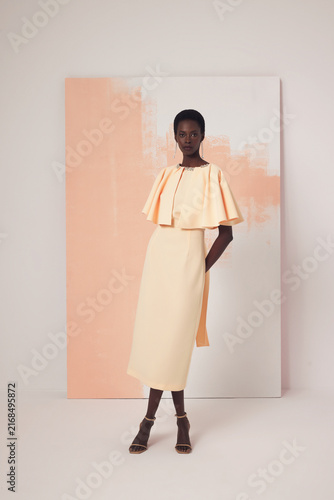 Cuadro en lienzo Black female model in pale peach midi dress with ruffled cape bodice