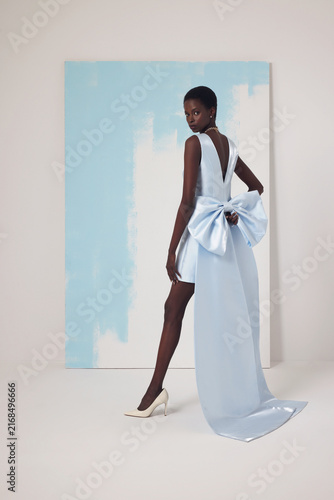 Fotografie Black fashion model in short light blue dress with massive floor-length train bo