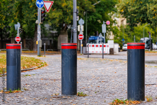 Konstfotografi Three black retractable bollards with red reflective stripes on cobblestone stre