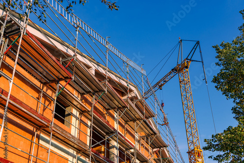 Residential building under construction with metal scaffolding and yellow tower crane against clear blue sky, real estate development concept
