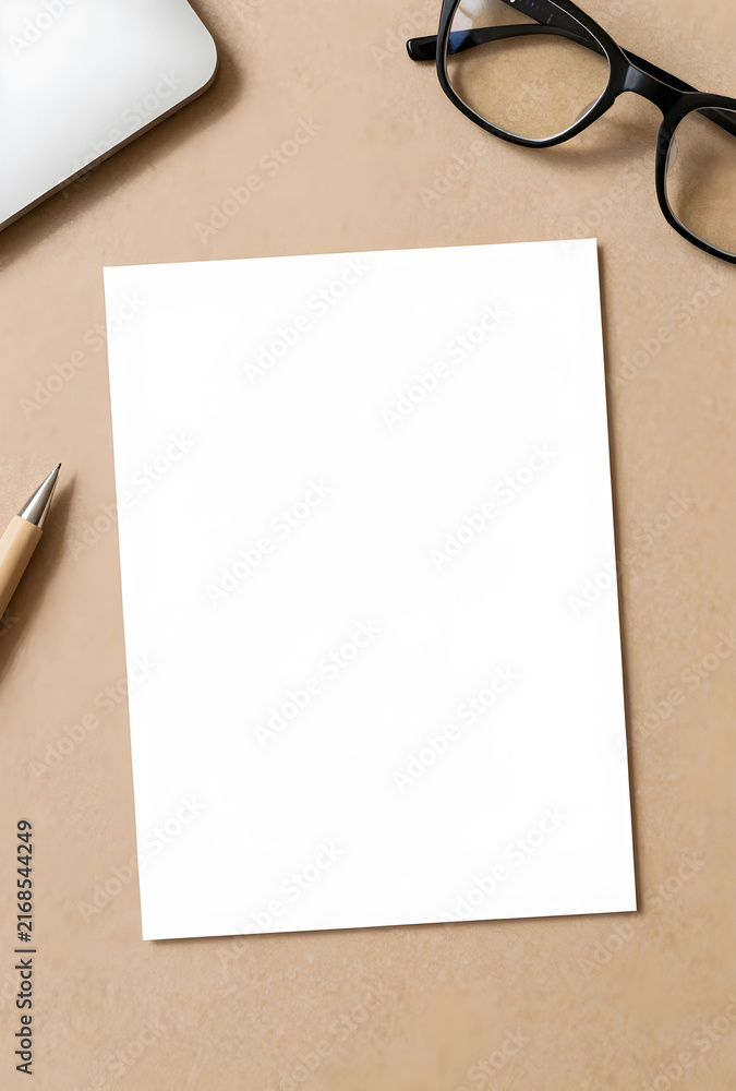 Fototapeta premium Blank white paper mockup on a brown desk with office supplies, copy space for text or design, top view flat lay