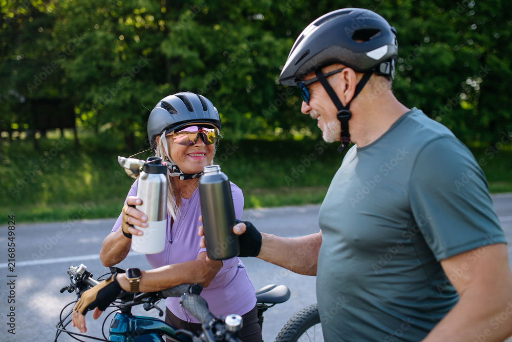 Fototapeta premium Mature couple resting and drinking water on bike tour.