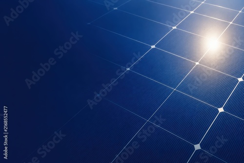 Close-up of solar panels reflecting sunlight under a clear blue sky, showcasing clean and renewable energy technology.