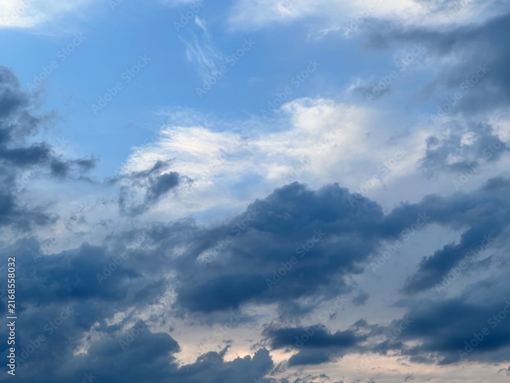 Fototapeta premium Dramatic blue sky with dark storm clouds and soft sunlight breaking through cloudy summer atmosphere