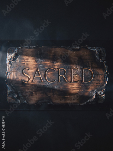 Wooden sign carved with word SACRED, rustic weathered typography on dark textured background