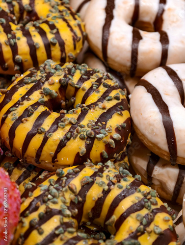 Fresh ring donuts with yellow glaze decorated with chocolate stripes and seeds arranged on a bakery display, featuring sweet baked pastries for customers