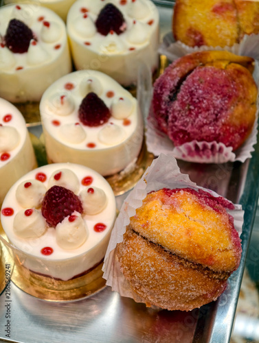 Sugar covered peach shaped pastries and white cream pastries with a real raspberry in the center form an attractive and varied dessert display in a confectionery shop