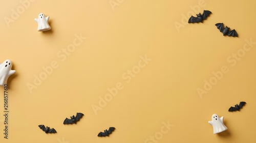 Cute halloween background with small ghosts and bats on a plain light orange paper surface