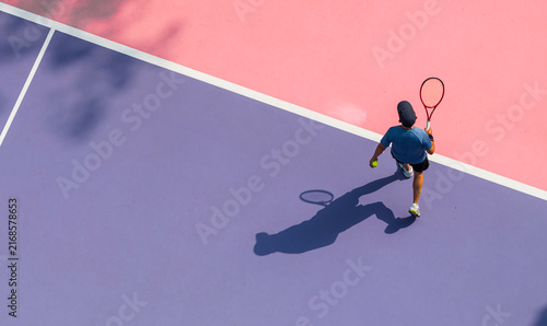 aerial view of a young tennis player in action on a vibrant pink and purple hard court. Dappled tree shadows and strong sunlight create a dynamic and aesthetic summer sports composition.