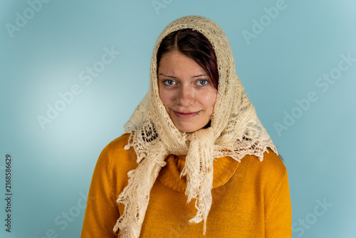 Obraz na płótnie Woman wearing a knitted wool shawl and sweater poses in front of a blue backgrou