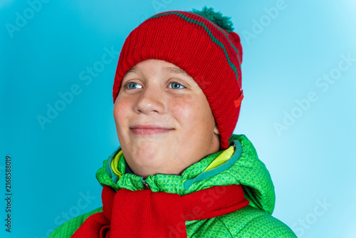 Boy wearing winter jacket, hat and scarf smiles in bright setting