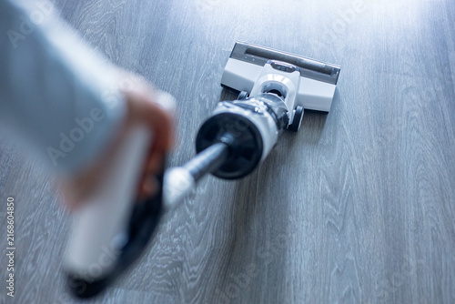 Person using a vacuum cleaner on wooden floor in a home during daytime