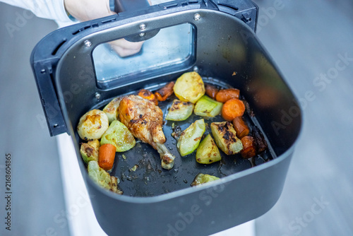 Cooking a meal in an air fryer with chicken, vegetables, and roots in a kitchen setting after preparation