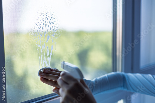 Person cleaning a window using a spray bottle and cloth during daylight in a bright indoor setting