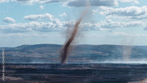 Smoke whirl spinning over burnt moorland on Llangynidr Moors, Brecon Beacons, charred earth and distant Welsh valleys under broken summer clouds