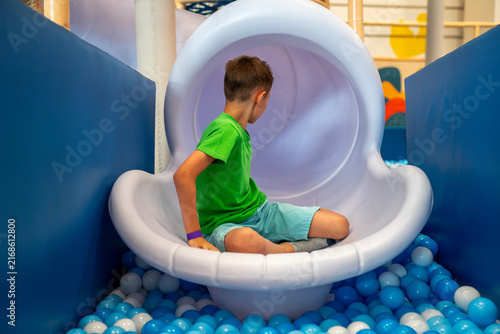Foto Boy sitting at bottom exit of white plastic tube slide above dry ball pit in indoor children entertainment playground center
