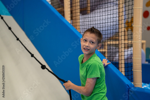 Foto Boy in green t-shirt holding a climbing rope on an inclined slope inside an indoor children play center, looking back