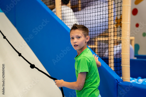 Foto Boy in green t-shirt holding a climbing rope on an inclined slope inside an indoor children play center, looking back