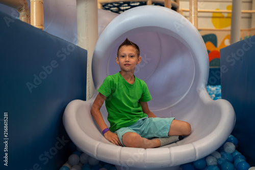 Foto Boy sitting at bottom exit of white plastic tube slide above dry ball pit in indoor children entertainment playground center