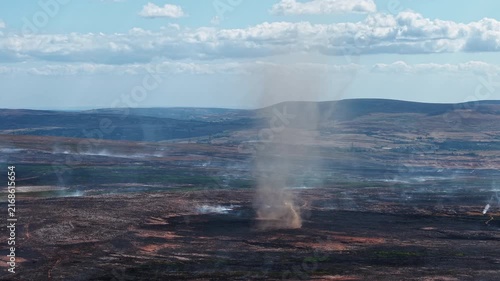 Smoke whirl and ash devil forming over scorched moorland after a wildfire, charred heathland smoldering under cumulus clouds on Llangynidr Moors in Wales