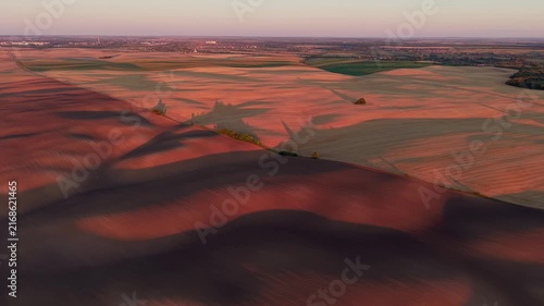 Magnificent aerial view of agricultural fields with rolling hills and beautiful long shadows from trees and clouds during a colorful sunset, creating a picturesque and tranquil rural landscape