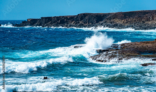 Fotografie Ocean waves crashing against a broad rocky shore