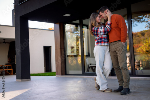 Young couple embracing and showing affection on a stylish patio outside their modern house, representing love, romance, and togetherness in a contemporary setting