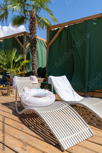 Fotografía Sun loungers on wooden deck with inflatable float ring and palm tree at beach cl