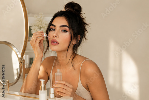 Beautiful woman applying facial serum with dropper during skincare routine