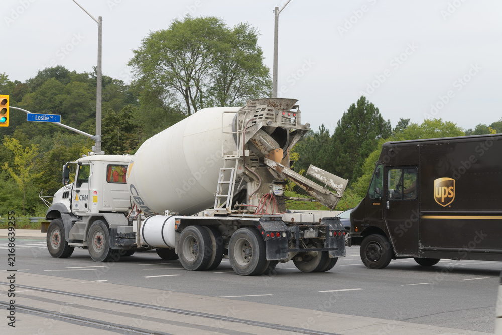Naklejka premium CBM (Canadian Building Materials) concrete mixer truck and UPS (United Parcel Service) delivery vehicle heading west on Eglinton Av E at Leslie St, Toronto