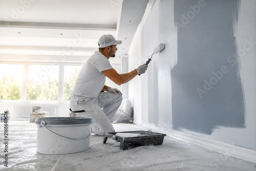Professional painter applying gray paint to an interior wall during home renovation