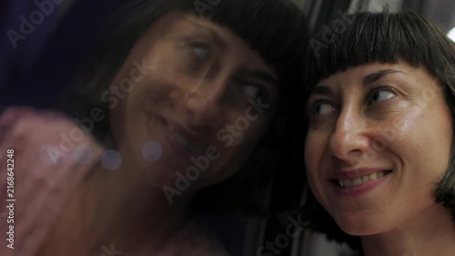 A young woman stares at the city lights at night, seeing through the train window. Her face is reflected in the train window as she travels through the metropolis. passenger of the train. girl in the 