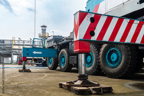 Принти на полотні A large mobile crane with red striped body and blue wheels deployed with outriggers extended at a petrochemical plant site in an industrial heavy equipment close-up shot