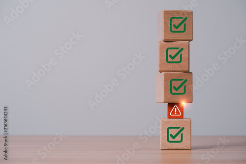 Risk management concept with warning symbol interrupting green check marks on stacked wooden blocks for compliance issues, quality control, audit, assessment and business problem detection.