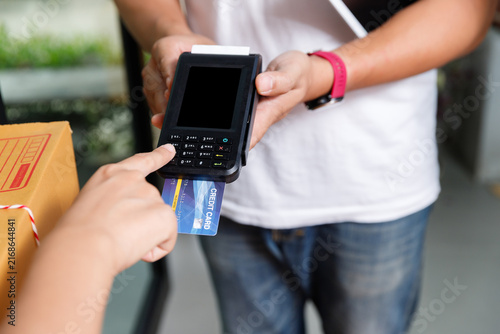Close up of hand making credit card payment via portable EDC terminal machine to delivery man at home. Modern digital banking and logistics concept.