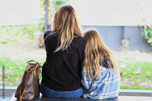 Принти на полотні A heartwarming scene of a mother and he little daughter sitting together on a stone bench, seen from behind