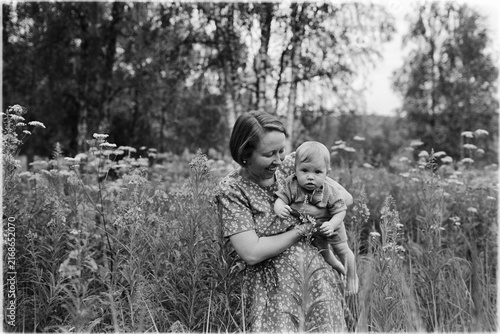 Black and white analog film portrait of a woman holding a baby in a field of wildflowers. Medium format grain is visible