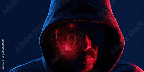 Hooded figure in darkness, illuminated by red light with a digital shield